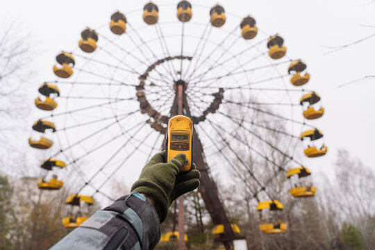 A man with a dosimeter in hand near ferris wheel. Abandoned amusement park in Pripyat city. Chernobyl Exclusion Zone.