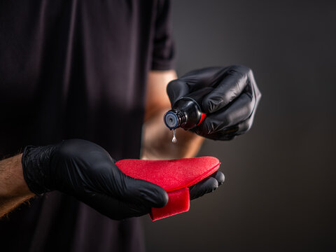 Gloved hands applying ceramic coating liquid onto red sponge for detailing, car ceramics liquid dropping