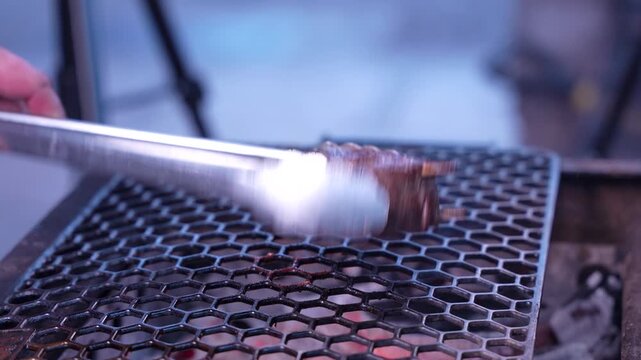 Close-up of beef filet mignon medallion cooking on a charcoal grill with hot embers, BBQ meat preparation outdoors. Juicy steak grilling over fire
