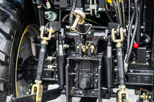 Close-up of complex mechanical structure, likely industrial tractor or heavy machinery, rendered in dark hues, intricate gears, axles, joints, metal or durable materials, no people, artificial ligh