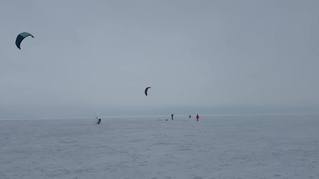 Kitesurfers riding on frozen lake with snow and overcast sky in winter landscape