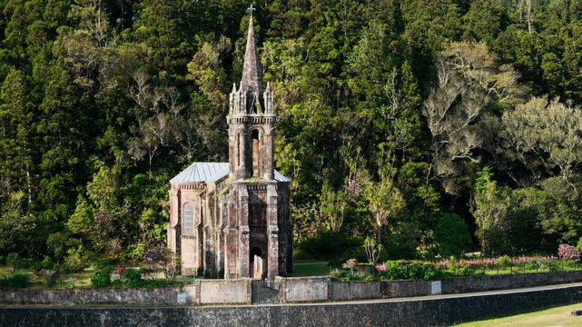 Aerial shot of stone chapel with tall spire against lush forest hillside in Azores