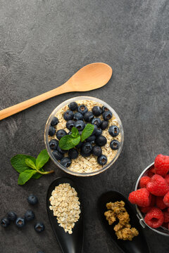 Yogurt Parfait with Blueberries, Oats and Mint in Glass Jar with Wooden Spoon and Raspberries on Dark Background &mdash; Healthy Breakfast Food Photography