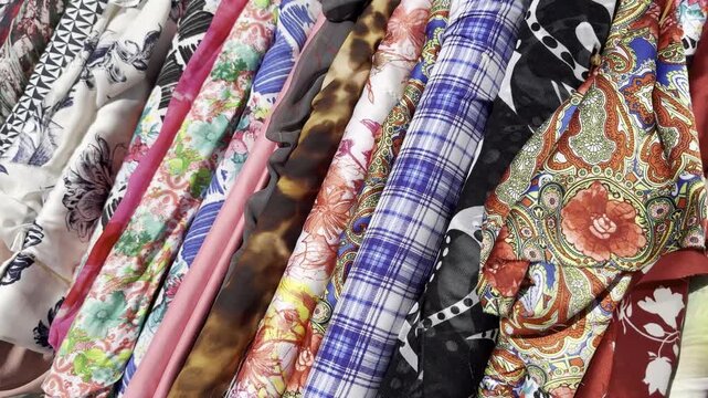 camera moving along colorful cotton and silk fabrics displayed outside shop in windy weather