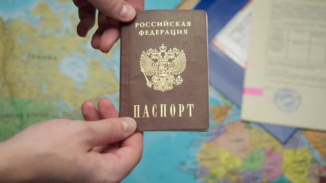 Close up shot shows migration officer handing over new Russian internal passport to citizen, with world map and approved documents with stamp creating official identification and residency