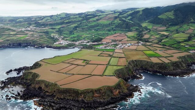 Volcanic cape with layered farmland terraces rising above rugged basalt cliffs on Atlantic shore of Sao Miguel, drone footage