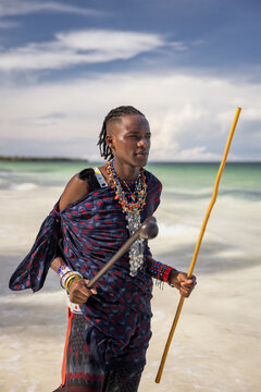 Portrait of a young Maasai man holding a rungu and a wooden stick on the beach in Zanzibar 