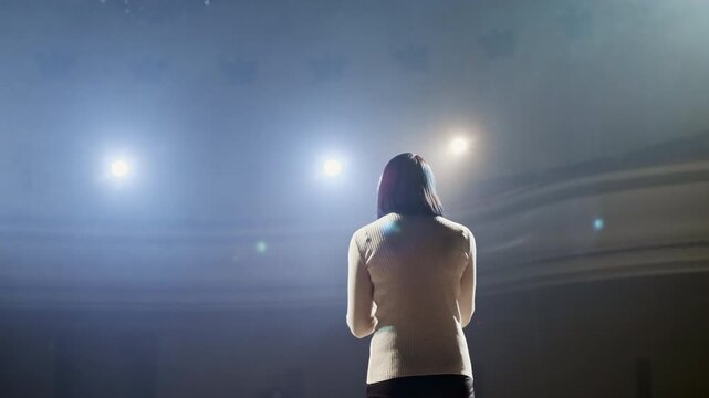 Young female actress performing a monologue on an empty stage, holding a script and rehearsing her lines with dramatic gestures under bright spotlights. The scene highlights focus, creativity, and