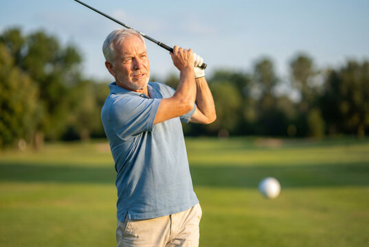 Senior man swinging golf club on green golf course