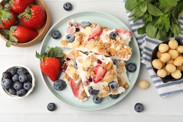 Fototapeta premium Pieces of tasty yogurt bark with berries, almond flakes and granola on light tiled table, flat lay