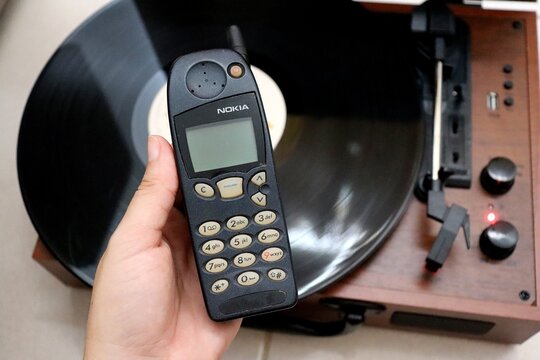 Salvador, Brazil - March 23, 2026: Woman's hand holding Nokia 5120 with retro vinyl turntable in the backgorund. 90s concept. Vintage home. 