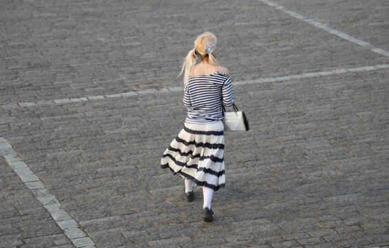back rear view of attractive crazy baby girl style freak blonde caucasian lady wear white handbag wear striped shirt with long sleeve striped skirt knee socks shoes cobbled floor flooring background