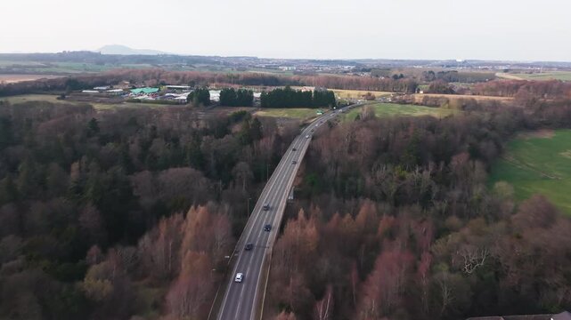 Road traffic on A7 passing through lush green forest and parkland near Melville in Midlothian, Scotland