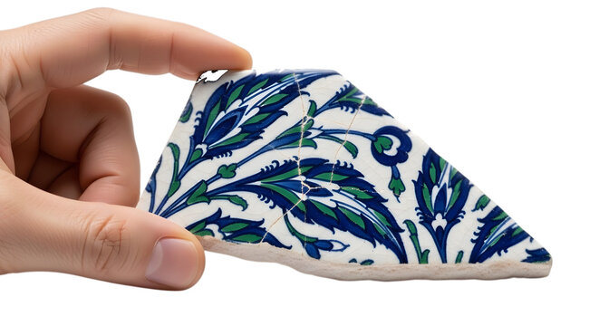 Hand holding ceramic tile fragment with blue green floral pattern