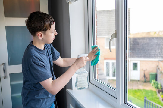 Teen boy cleaning window with cloth at home, helping with chores, responsibility learning, everyday routine.