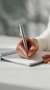 A hand holds a sleek pen, jotting notes in a lined notebook, symbolizing planning and organization. The bright workspace evokes focus, learning, and inspiration