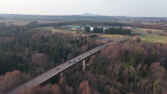 Aerial perspective of a road bridge passing through lush green forest and parkland near Melville, Scotland