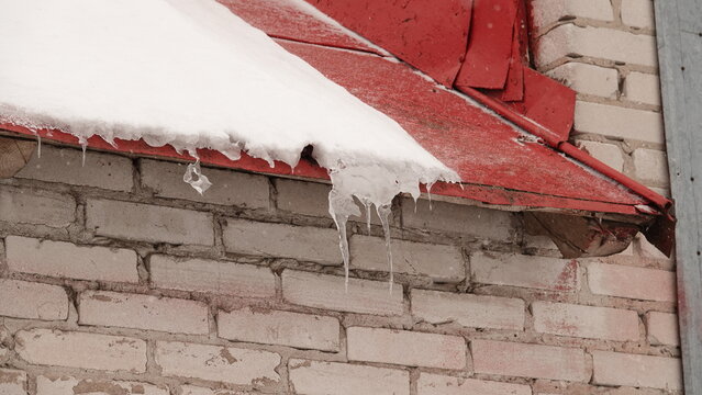 Długie sople lodu zwisające z dachu budynku gospodarczego