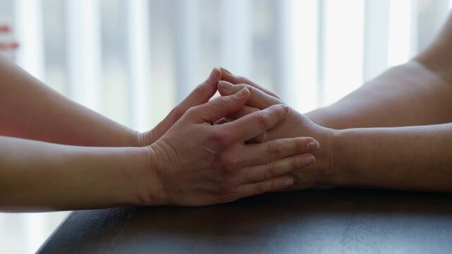 Close up shot of Granddaughter gently holding her Grandmother hands across a table, expressing love, care, family support, and intergenerational connection.