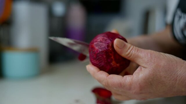 Close up view of Hands Peeling Beetroot with Knife in Kitchen