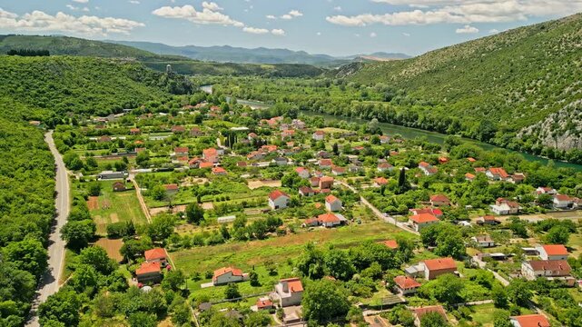 Bosnia and Herzegovina - 05 17 2025: Tracking drone video of Počitelj village, showing terracotta rooftops, winding road, lush greenery, Neretva River, rolling hills, and blue sky on a sunny day