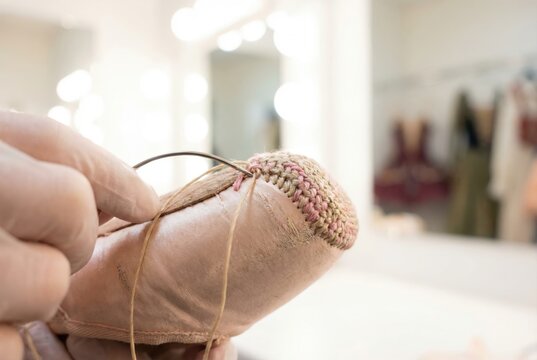 Ballerina hand sewing a protective darned edge onto the tip of a pink satin pointe shoe with a needle