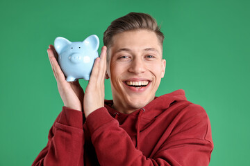 Fototapeta premium Happy man with piggy bank on green background