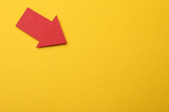Red paper arrow on yellow background, top view. Space for text