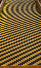 Fototapeta premium Close-up of a yellow and black diagonal striped warning surface on a walkway or ramp. Industrial safety pattern with strong graphic lines and worn texture, suitable for backgrounds, hazard concepts