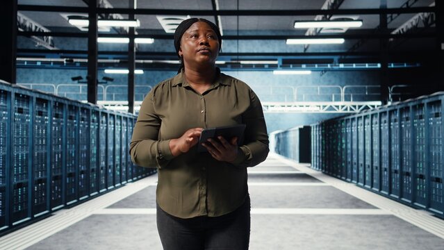Data center employee using tablet to manage software updates for system stability. African american engineer in server room configuring infrastructure with device for optimum performance, camera A