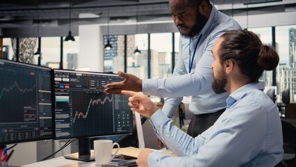 Prop firm staff members communicate at PC desk to ensure smooth trading operations. Team of traders in office doing brainstorming, discussing market trends and portfolio positions © DC Studio