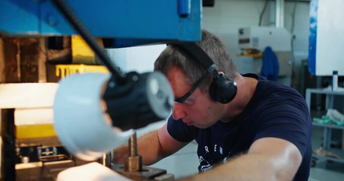 Male factory worker performing metal stamping operation at industrial press. Manufacturing labor and workshop activity
