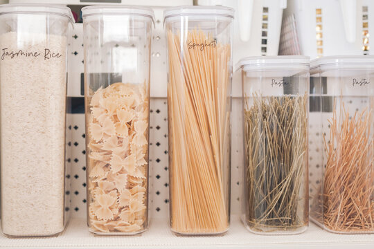 Pantry organization kitchen storage food containers organized kitchen jasmine rice spaghetti dry pasta and various noodles in clear airtight labeled canisters on a pantry shelf.