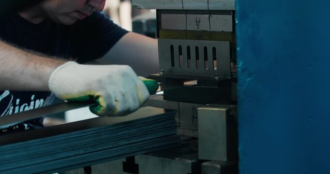 Blue collar worker operating press machine in metal stamping workshop. Factory labor and industrial production process