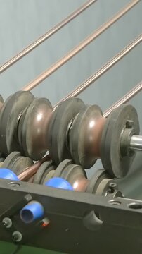 Gleaming copper tubes advance steadily through powerful rollers on an intricate industrial machine.