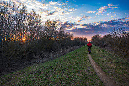 Cyclist on grassy levee near Warsaw rides toward sunrise or sunset