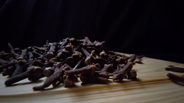 Cinematic macro of dried Cloves on a wooden surface. Intense lighting highlights the rich texture and natural detail against a dark background. Ideal for culinary and wellness