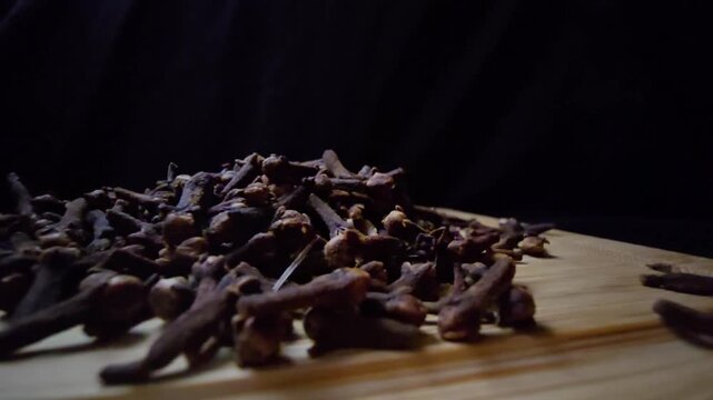 Cinematic macro of dried Cloves on a wooden surface. Intense lighting highlights the rich texture and natural detail against a dark background. Ideal for culinary and wellness