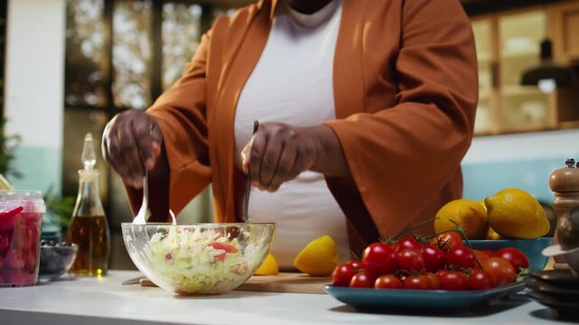 Food content creator recording high quality video preparing a salad, meal prep at the kitchen counter. Black woman influencer prepares delicious gourmet dish, guiding audience through recipe.