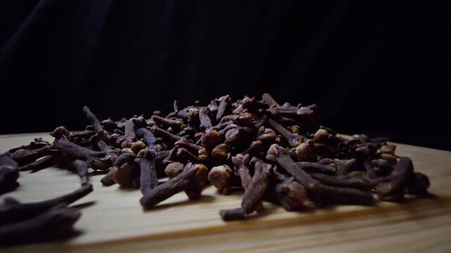 Cinematic macro of dried Cloves on a wooden surface. Intense lighting highlights the rich texture and natural detail against a dark background. Ideal for culinary and wellness
