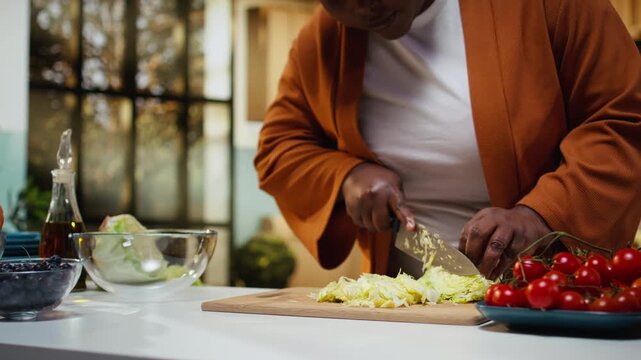 Black food blogger cutting iceberg salad on the cutting board, doing meal prep for a fresh salad bowl. Woman recording a culinary tutorial vlog at home kitchen, social media platforms.
