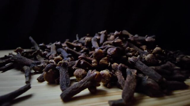 Cinematic macro of dried Cloves on a wooden surface. Intense lighting highlights the rich texture and natural detail against a dark background. Ideal for culinary and wellness