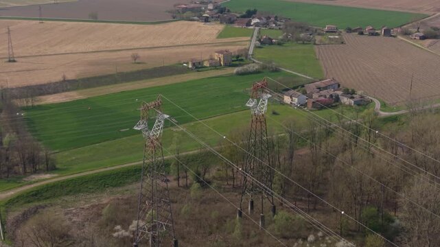 An aerial view showcases the intersection of nature and industry, with power lines stretching across a patchwork of cultivated fields and green spaces. Emilia Romagna, Piacenz