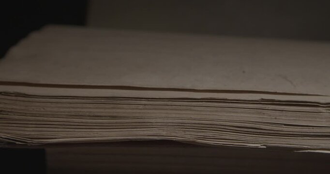 Closeup of pages of an old weathered vintage book in local light. Historical knowledge archive library concept. Hand turn the pages stuck together. Slider macro 4K video.