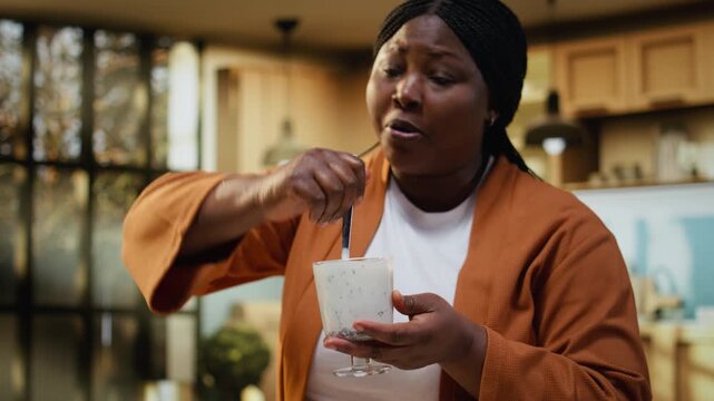 Female food vlogger mixing nutritious chia seeds yogurt bowl in home kitchen. Content creator filming under natural light to create protein rich breakfast idea for online audience and channel.