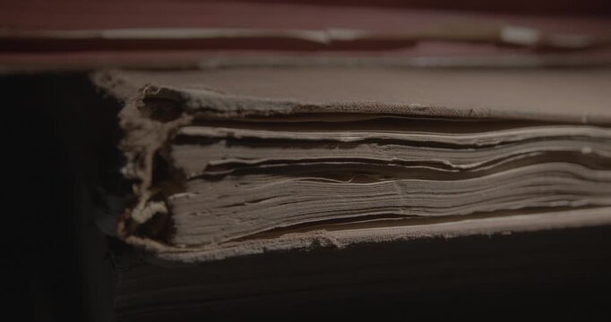 Closeup of pages of an old weathered vintage book in local light. Historical knowledge archive library concept. Slider macro 4K video.
