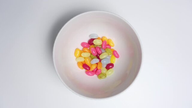 Loop stop motion of colorful jelly beans disappearing and reappearing in a white bowl, top view, minimal flat lay, endless cycle concept