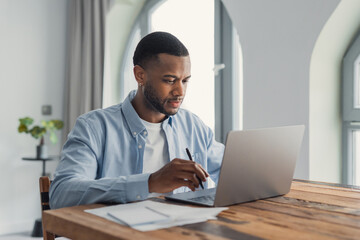 Fototapeta premium Man working on laptop at home office desk focused on remote work and paperwork
