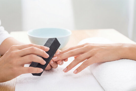 Professional manicurist filing nails of client in beauty salon