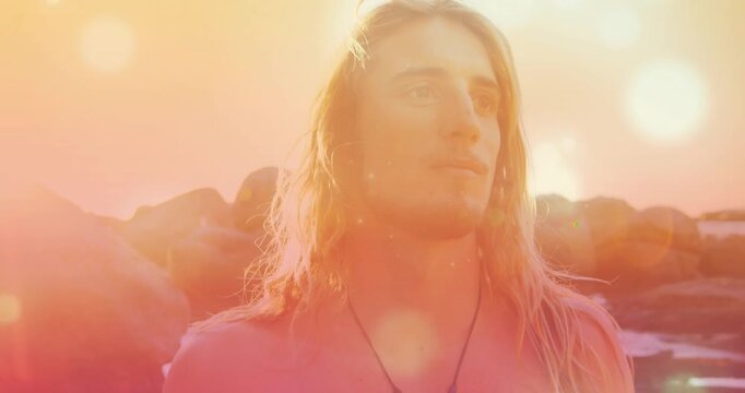 Shirtless man turning gaze toward rocky shore camera closing in revealing pendant sunflare for film